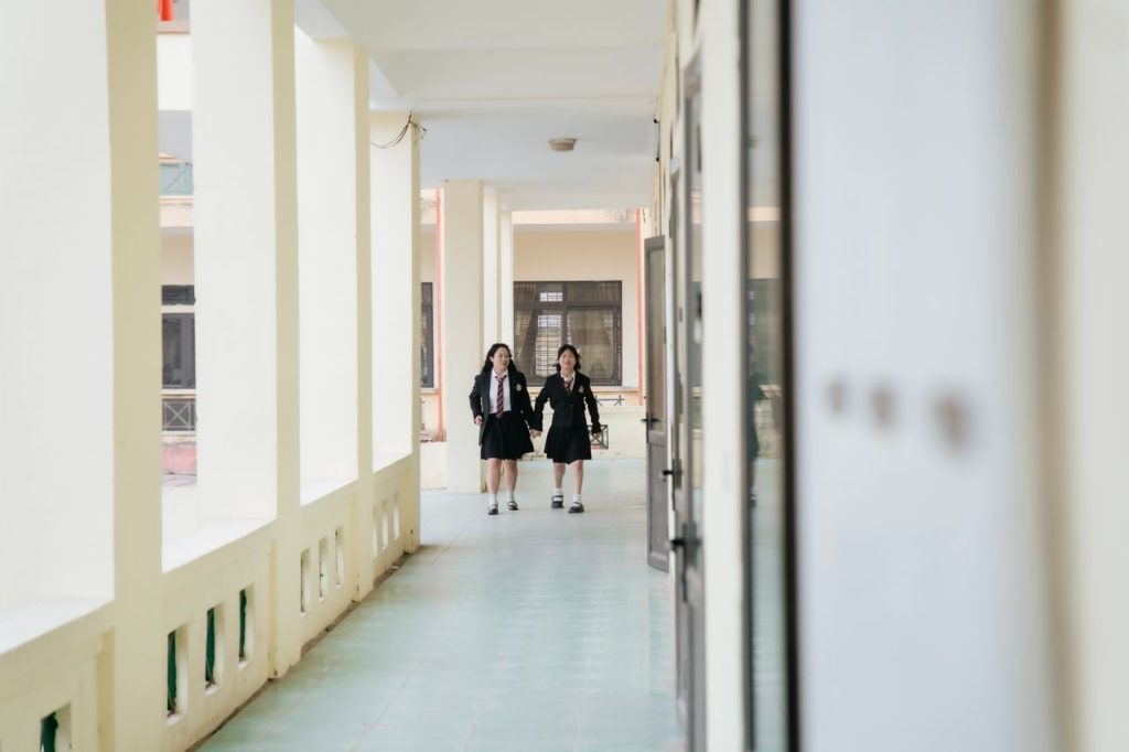 Two students in uniform walk through a bright school corridor.